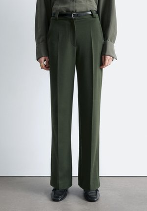 Skræddersyede bukser i olivengrøn med læg, kombineret med sort bælte, mørke oxford-sko og matchende olivengrøn skjorte med lange ærmer.