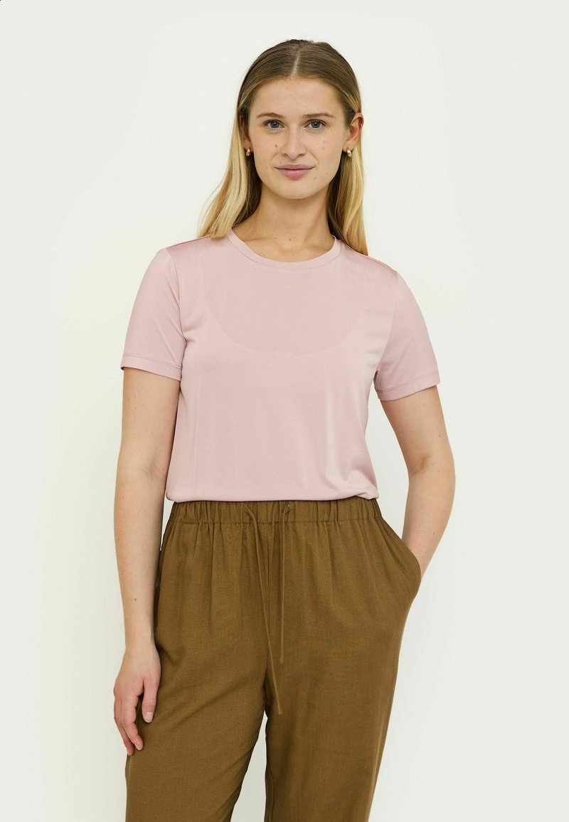 T-shirt rose clair à manches courtes et col rond, fabriqué en tissu doux, associé à un pantalon marron à taille élastique et coupe fuselée. Aucun motif visible.