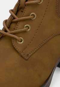 Gros plan sur une botte en cuir marron avec des lacets ronds assortis passant à travers des œillets en laiton et une couture détaillée.