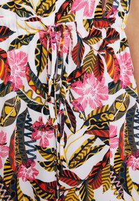 Tissu à motifs floraux avec des fleurs roses et jaunes, des feuilles vertes et noires, et des liens noirs à la taille. Matériau léger et texturé.