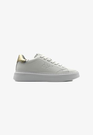 Sneaker bianco in pelle con suola spessa bianca. Presenta un accento metallico dorato nel tallone e un dettaglio del logo sul lato. Include i lacci.