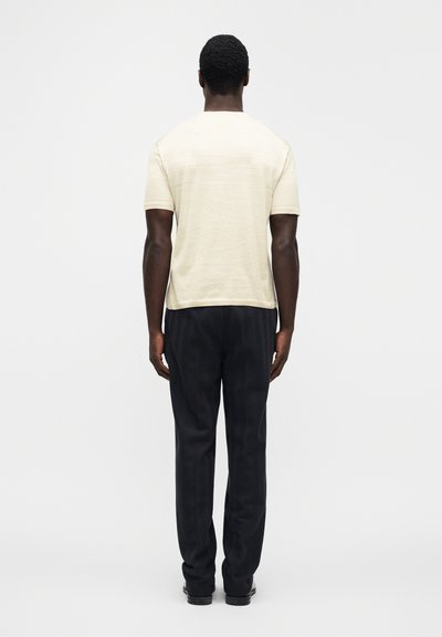 Μπεζ πουκάμισο με κοντά μανίκια και υφή, συνδυασμένο με σκούρο παντελόνι με σχέδια, από πίσω. Λείες υφές σε όλο το ρούχο.