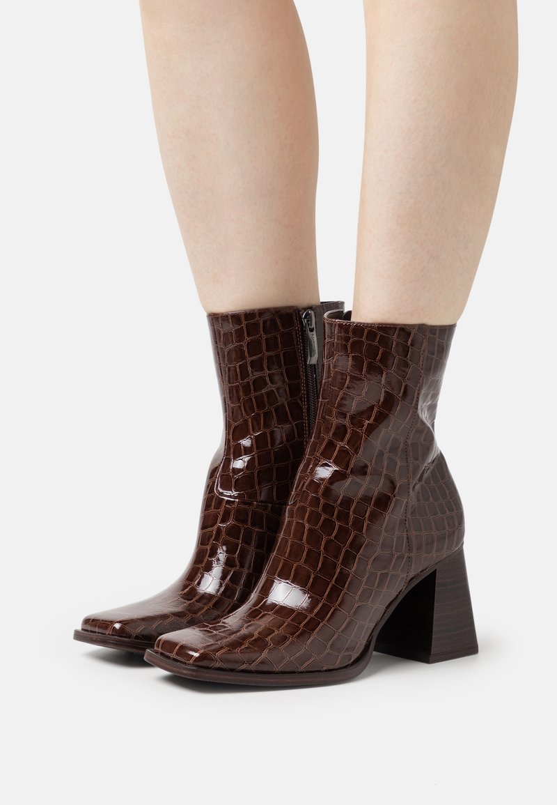 Bottines en cuir verni marron avec une texture crocodile, bout carré, fermeture éclair sur le côté et un talon épais.