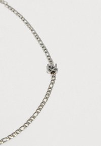 Ασημένιο μεταλλικό κολιέ με στρογγυλούς κρίκους, που διαθέτει ένα κεντρικό μενταγιόν με ανάγλυφο το "HUGO". Λείο υφή, μίνιμαλ σχεδιασμός.