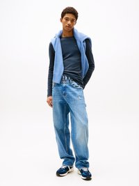 Blå langtermet skjorte, lyseblå strikkegenser drapert, slitte lyseblå jeans og marineblå sneakers med hvite detaljer. Hvit bakgrunn.