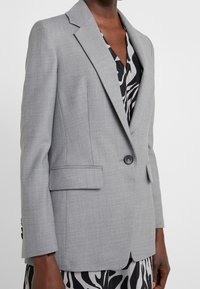 Personne à la peau foncée portant un blazer gris clair cintré sur une robe à motif noir et blanc avec un imprimé zèbre.