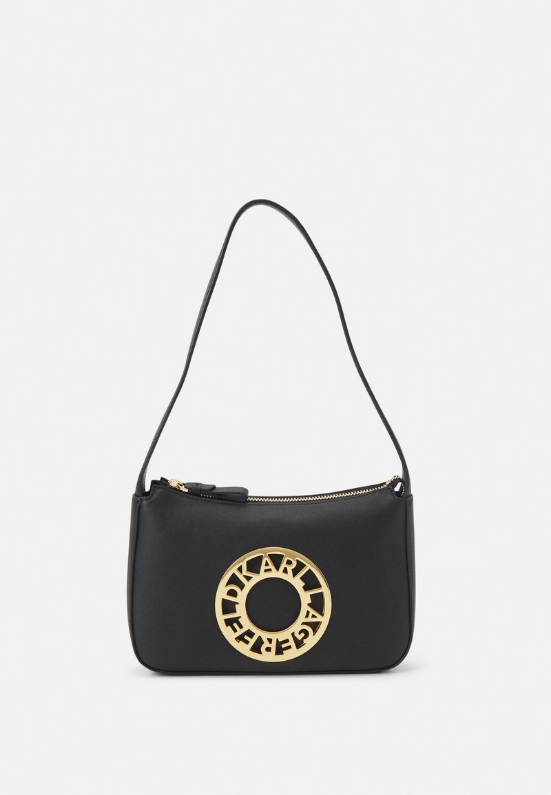 Sac à main en cuir noir avec fermeture éclair, arborant un logo circulaire doré bien en vue, une texture lisse et une sangle slim, réglable.