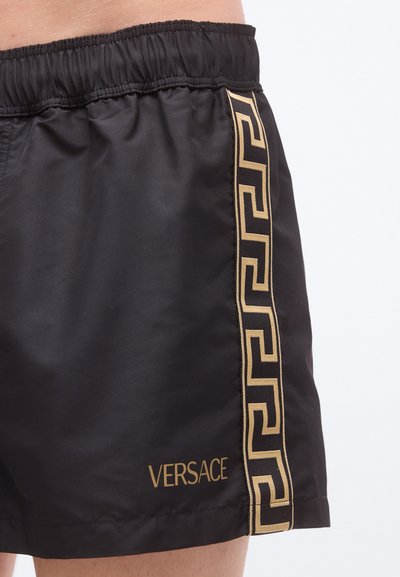 Μαύρα μαγιό σορτς από λείο υλικό με χρυσό μοτίβο ελληνικού κλειδιού στο πλάι και το λογότυπο "VERSACE" στο τελείωμα.