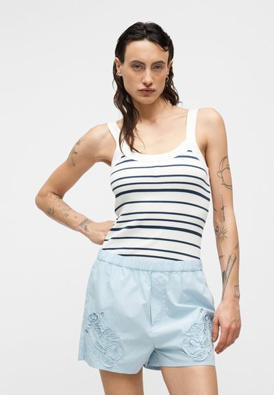 Ριγέ αμάνικη μπλούζα σε λευκό και ναυτικό μπλε, συνδυασμένη με ανοιχτό μπλε σορτς με κεντημένες αστακούς. Λείο ύφασμα, casual σχέδιο.