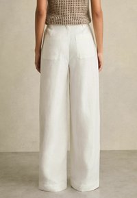 Weiße Leinenhose mit weitem Bein und hoher Taille, ausgestattet mit zwei Gesäßtaschen und einer weichen, strukturierten Oberfläche.