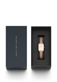 Orologio rettangolare in oro rosa con cinturino in maglia, esposto in una scatola blu scuro con interno nero. Marchio visibile sulla scatola.