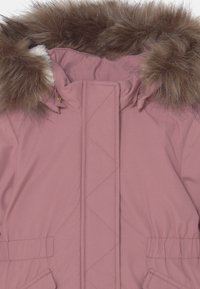 Veste matelassée rose avec un bord de capuche en fausse fourrure, poignets élastiques et poches frontales. Le matériau semble doux et résistant aux intempéries.