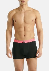 Svarta boxershorts med en rosa midja som har en logotyp och randig design. Tyget ser slätt och åtsittande ut.