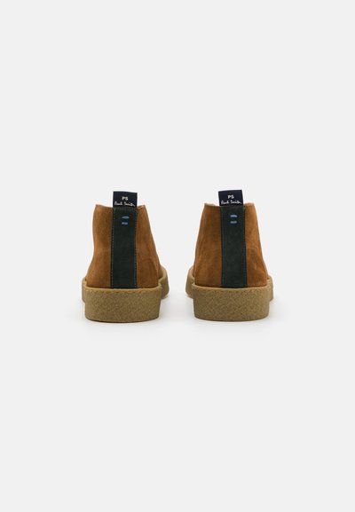 Braune Wildleder-Ankle-Boots mit grünen Seitenpaneelen, strukturierten Gummisohlen und einem navyblauen Zugband hinten. Schlichtes und modernes Design.