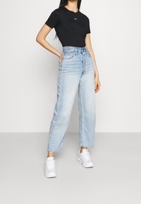 Svart åtsittande t-shirt med en liten vit Nike-logotyp, ihop med högmidjade, ljusblå raka jeans och vita sneakers.