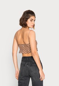 Top crop castanho com bolinhas brancas, com alças finas e bainha franzida, combinado com jeans pretos de cintura alta, mostrando uma vista traseira.