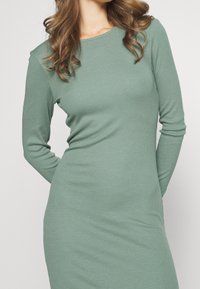 Abito a maniche lunghe in rib Rame, di un verde morbido e tenue. Presenta un coltondo e una silhouette aderente. Realizzato in tessuto elasticizzato per il massimo comfort.