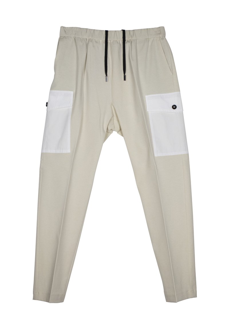 Beige elastische broek met een losse fit, voorzien van witte patchzakken aan de zijkanten, zwarte trekkoorden en knoopaccenten op de zakken.