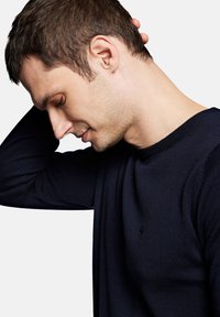 Granatowy sweter z okrągłym dekoltem, wykonany z teksturowanej dzianiny, z małym logo na piersi. Dopasowany fason podkreśla linię szyi i ramion.