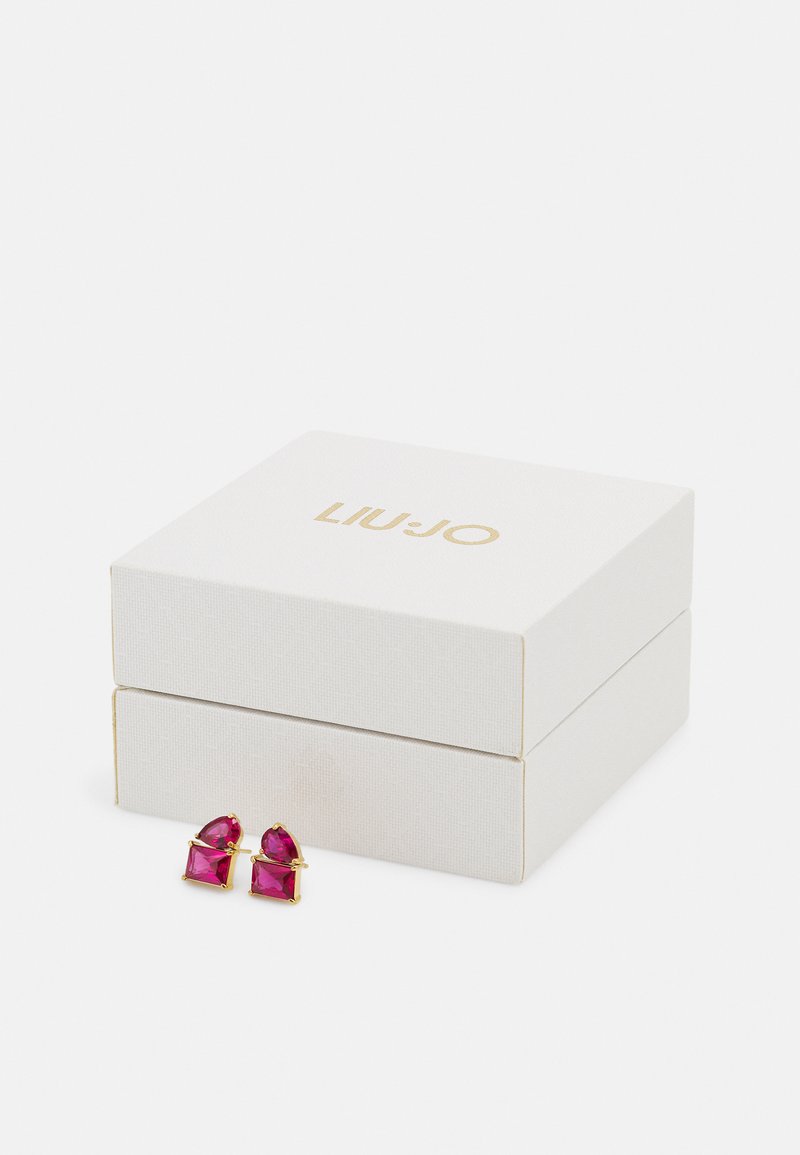 Orecchini con accenti dorati che presentano gemme rosa in due forme, esposti accanto a una scatola regalo bianca testurizzata con lettere dorate.
