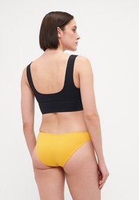Svart, ermeløs sports-bh med bred scoop rygg, kombinert med gule bikini-truser, glatt tekstur og minimale sømmer.