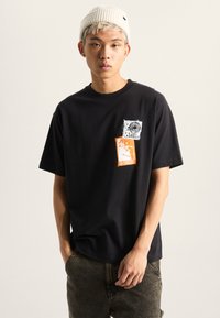Sort bomulds t-shirt med korte ærmer, der har livlige grafiske prints i hvid og orange. Løs pasform, rund halsudskæring og glat tekstur.