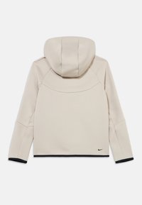 Φωτεινή μπεζ φούτερ με κουκούλα, εφαρμοστή γραμμή, μαύρα ριμπ μανσέτες και διακριτικό λογότυπο Nike στο κάτω δεξί μέρος. Μαλακή υφή.
