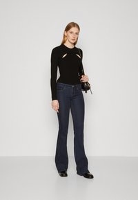 Svart langermet topp med utskjæringer, kombinert med mørkeblå buksene med vide ben. Enkel design, myk tekstur og tettsittende silhuett.