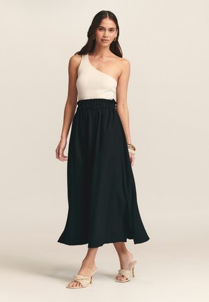 One-shoulder ribbed cream top paired with a black, flowy maxi skirt featuring an elastic waist. Worn with braided beige heeled sandals.