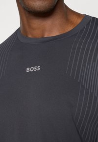 Σκούρο γκρι αθλητικό μπλουζάκι με υφή, που διαθέτει διακριτές �κάθετες ρίγες, στρογγυλή λαιμόκοψη και το λογότυπο "BOSS" σε ασημί πλέξη.