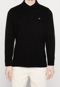 Schwarzes Langarm-Polohemd mit Kragen, ausgestattet mit einer zweiknöpfigen Knopfleiste und einem kleinen gestickten Logo auf der Brust. Weicher Stoff, lässige Passform.