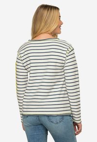 Maglione a righe bianco con linee blu navy, presenta una vestibilità rilassata, collo rotondo e un accento giallo sulla manica sinistra. Materiale a maglia testurizzata.