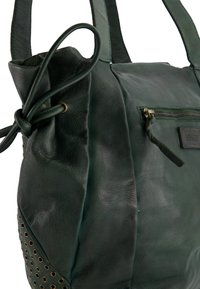Groene leren handtas met een textuur, trekkoordsluiting, een voorvak met rits en decoratieve metalen oogjes aan één zijde.