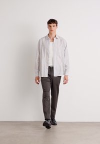 Lightweight, long-sleeve shirt with a vertical striped pattern in pale colors, paired with gray trousers and black shoes, on a neutral background.