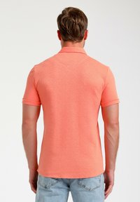 Korte mouwen polo in een gestructureerde fel koraalkleurige stof met een klassieke kraag en opgerolde mouwen, gecombineerd met lichtblauwe denim jeans.