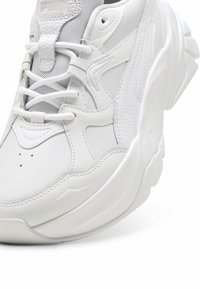 Białe sneakersy z mieszanką gładkiej i teksturowanej skóry, panelami siatkowymi oraz masywną podeszwą z zakrzywionymi akcentami. Sznurowane z przodu.