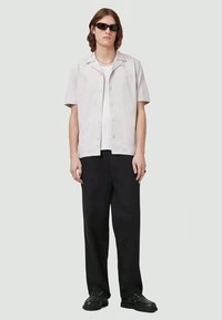 Camisa de botão de manga curta, cinza claro, com um corte relaxado, combinada com calças largas pretas e sapatos pretos. Óculos de sol usados.