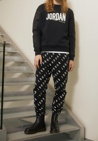 Felpa nera con logo "JORDAN", abbinata a pantaloni della tuta neri con stampa ripetuta "JORDAN" e stivaletti neri con suole chunky.