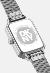 Zilveren roestvrijstalen horloge met een rechthoekige wijzerplaat, mesh band en DKNY-logo op de achterkant. Waterbestendig tot 3 ATM.