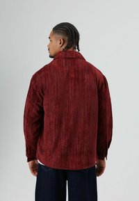 Corduroy overhemd in bordeauxrood met een zichtbare geribbelde textuur, grote kraag en een ontspannen pasvorm, voorzien van lange mouwen en zijslitten.