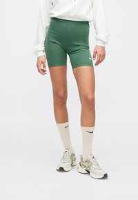 Πράσινα σορτς από βαμβακερό μείγμα με εφαρμοστό σχέδιο, συνδυασμένα με μπεζ κάλτσες Nike και αθλητικά παπούτσια με λεπτομέρειες και λογότυπο.