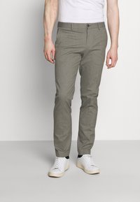 Pantalones grises ajustados confeccionados en un tejido ligero, con un frente plano, bolsillos laterales y un corte slim, combinados con zapatillas blancas.