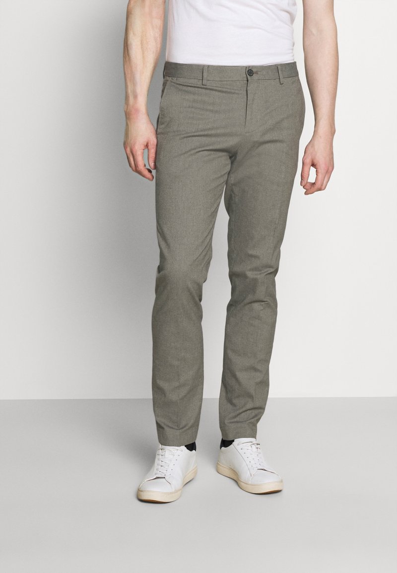 Pantalones grises ajustados confeccionados en un tejido ligero, con un frente plano, bolsillos laterales y un corte slim, combinados con zapatillas blancas.