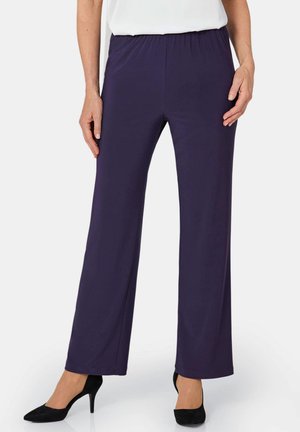 Pantalons violets extensibles avec une taille élastique, une coupe large et une texture lisse, associés à des chaussures à talons hauts noires.