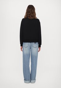 Zwarte cropped sweatshirt met ronde hals, gecombineerd met lichtblauwe, loszittende geputeerde jeans met achterzakken en zichtbare stiksels.