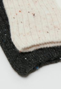 Due sciarpe di lana lavorate a maglia: una di un crema chiaro con macchie colorate, l'altra grigia scura con una finitura texturizzata e fibre visibili.