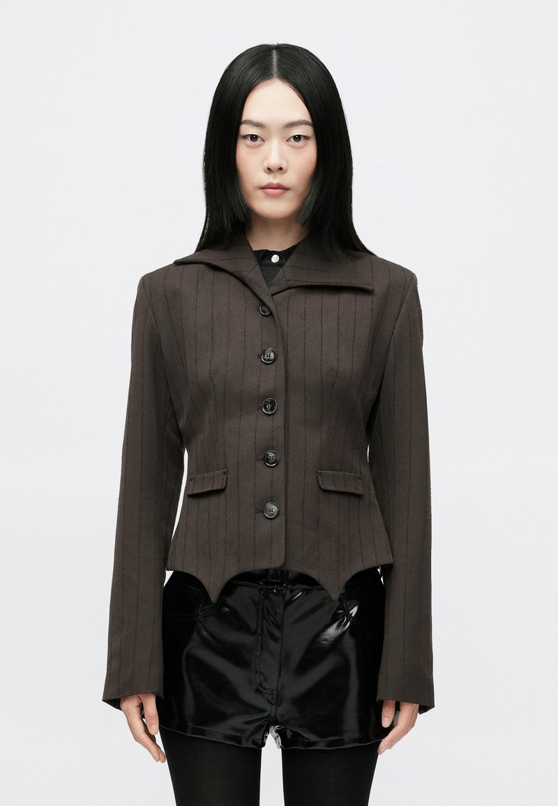 Barna csíkozott blazer, lekerekített gallérral, hat fekete gombbal és két elülső zsebbel. Az alja aszimmetrikus. Fekete rövidnadrág felett viselik.