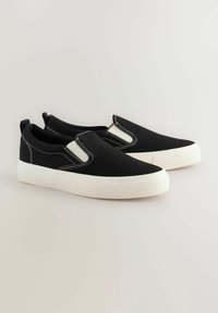 Mustad musta kangast slip-on jalatsid, millel on elastsed servad, valged õmblused ja tekstuuritud kummist tallad, disainitud igapäevaseks kandmiseks.