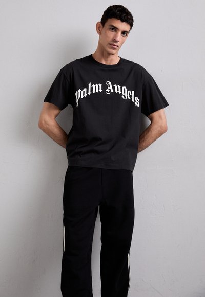 Zwarte katoenen t-shirt met korte mouwen, voorzien van witte "Palm Angels" tekst in Gothic-lettertype. Gecombineerd met zwarte sweatpants met zijstrepen.
