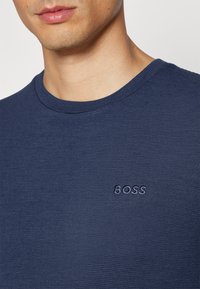Camiseta de algodão azul marinho com uma textura canelada e um decote redondo, apresentando um logótipo bordado "BOSS" no lado esquerdo do peito.